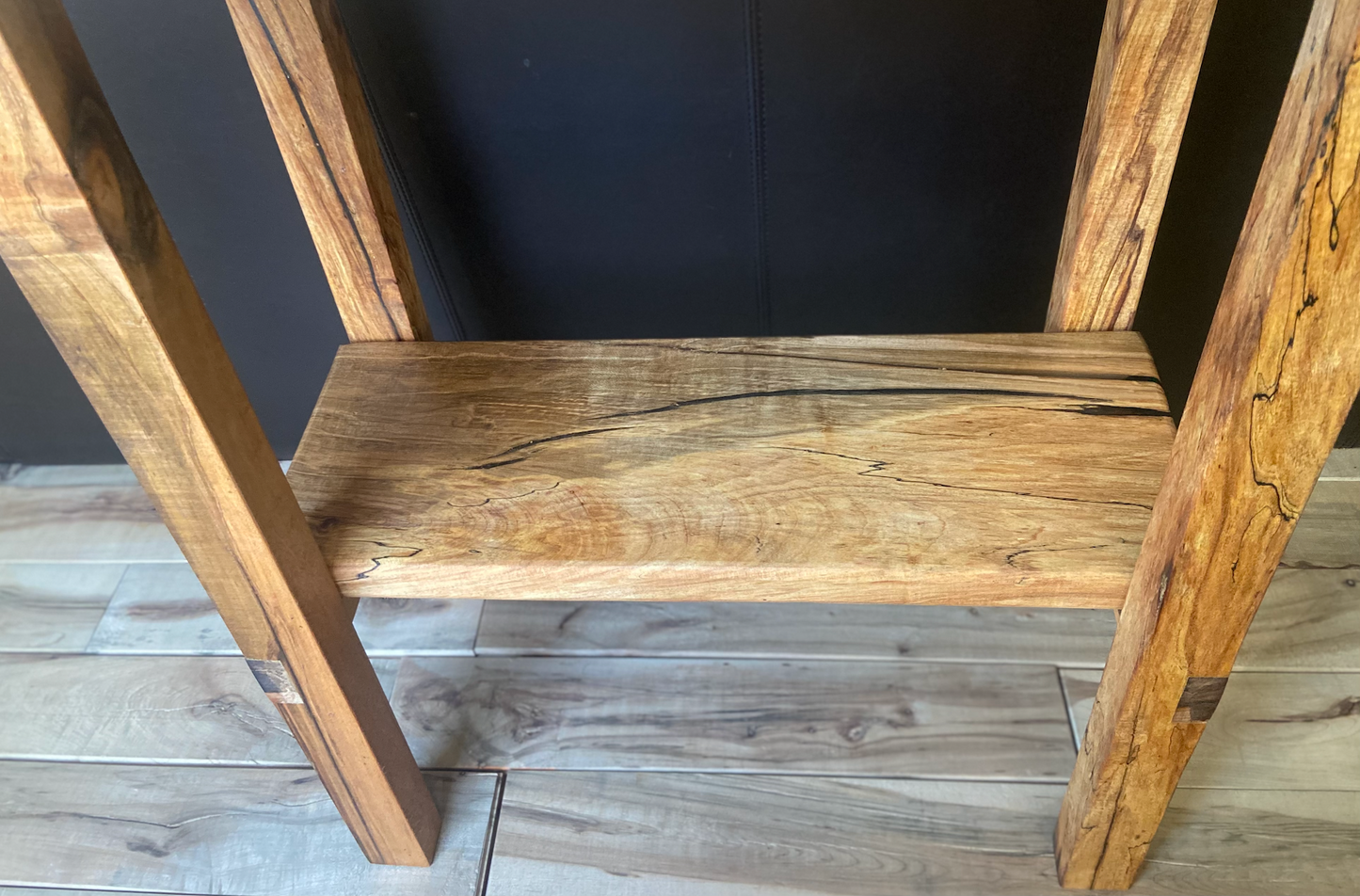 Top-down and close up view of spalted maple sofa or console table, highlighting natural wood grain, warm tones, and wood details. Handcrafted spalted maple console / sofa table styled in a modern living room with a cozy, rustic aesthetic. Detailed view of spalted maple wood grain, showing natural spalting, color variations, and organic patterns. Straight edge entryway table made from spalted maple, featuring unique grain patterns and a smooth, polished surface. Rustic and modern design.