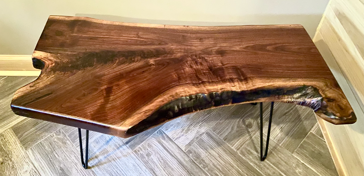 Live edge walnut wood slab coffee table with a natural edge design on a gray floor.