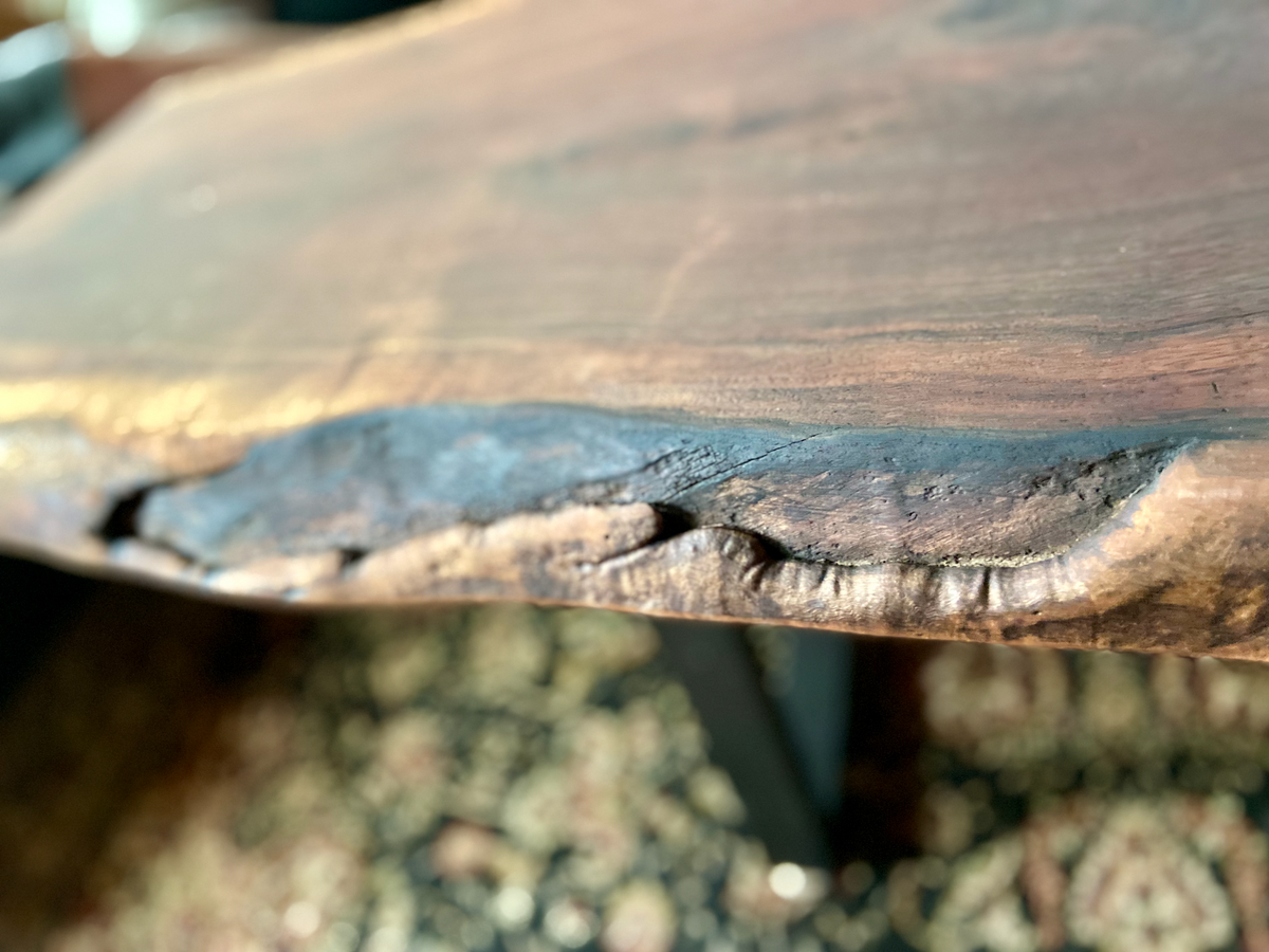 Close up view of large live edge black walnut coffee table, highlighting natural wood grain, and live edge details. Handcrafted live edge walnut coffee table styled in a modern living room with a cozy, rustic aesthetic. Detailed view of live edge walnut wood grain, showing natural color variations, and organic patterns. Large live edge black walnut coffee table made from walnut featuring unique grain patterns and a smooth, polished surface. Rustic and modern design.