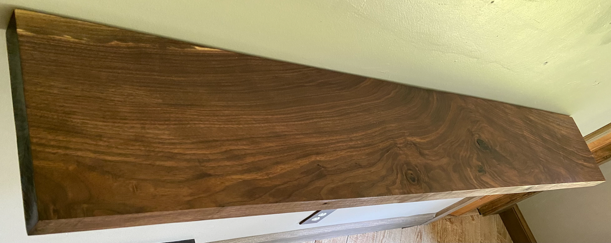 Front view of a handcrafted straight edge black walnut floating shelf mounted on a wall, displaying decorative items. Close-up of the solid black walnut wood grain, highlighting the shelf’s smooth finish. Side angle showcasing the shelf’s thickness and sturdy wall brackets.