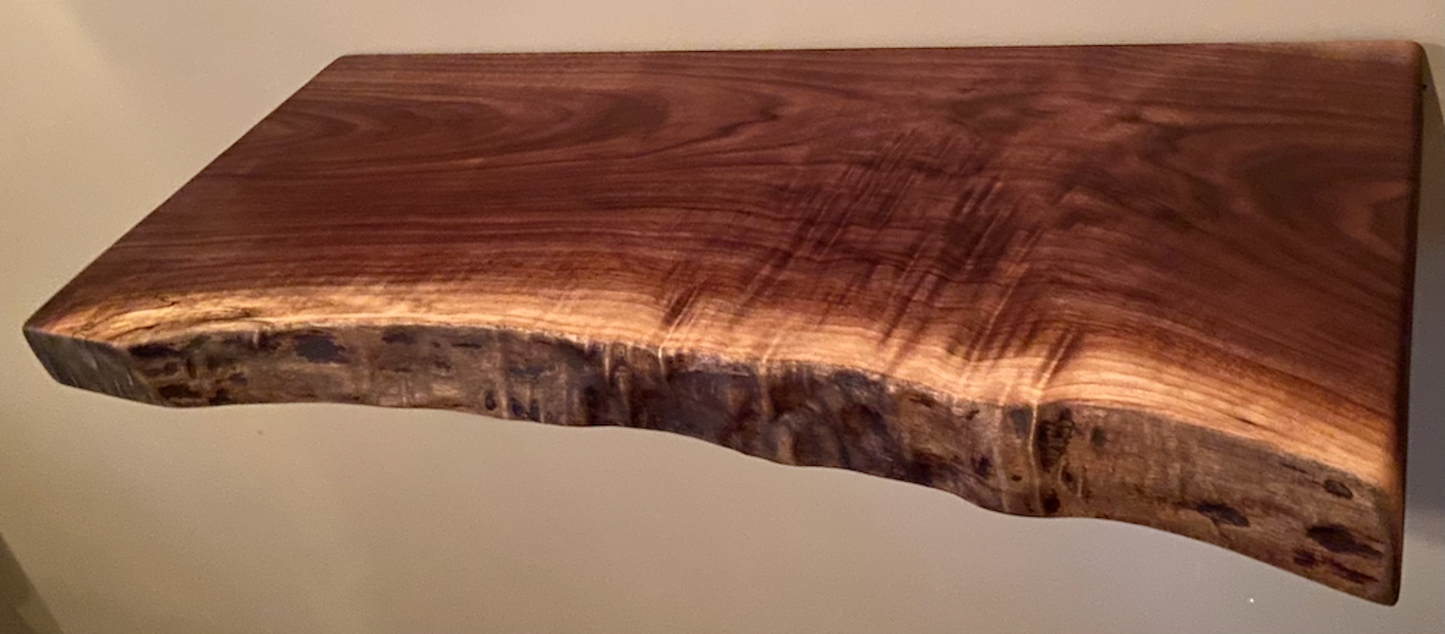 Live edge walnut floating shelf mounted on a light-colored wall, showcasing natural grain, dark tones, and organic edge detail