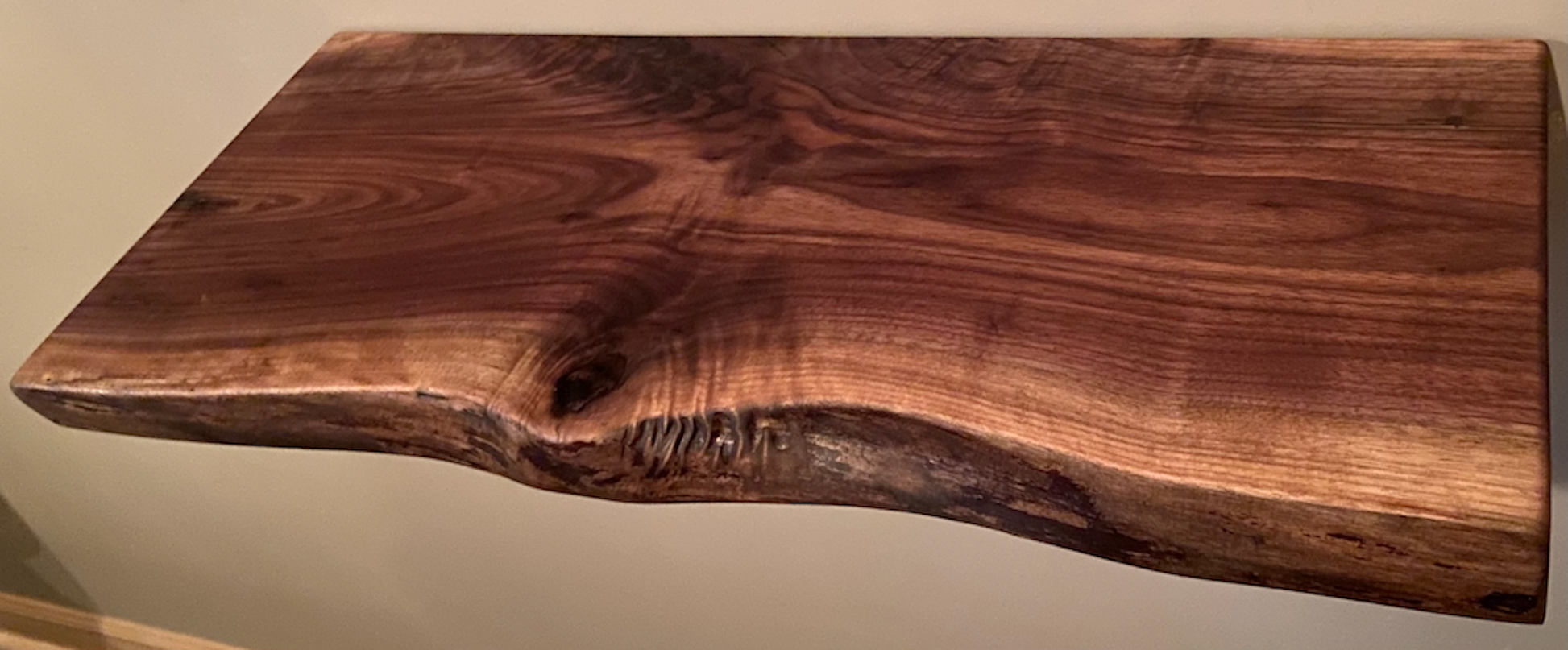Live edge walnut floating shelf mounted on a light-colored wall, showcasing natural grain, dark tones, and organic edge detail