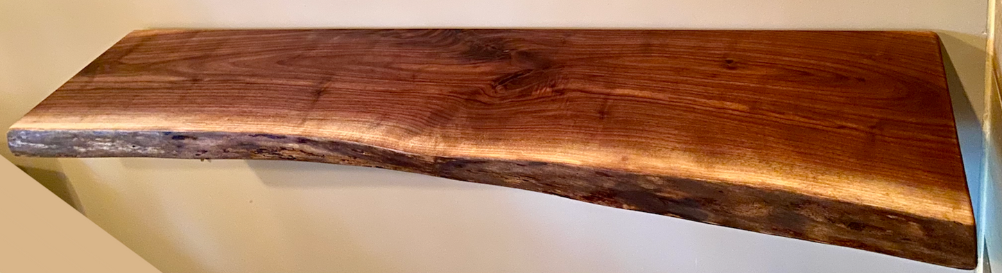 Live edge walnut floating shelf mounted on a light-colored wall, showcasing natural grain, dark tones, and organic edge detail
