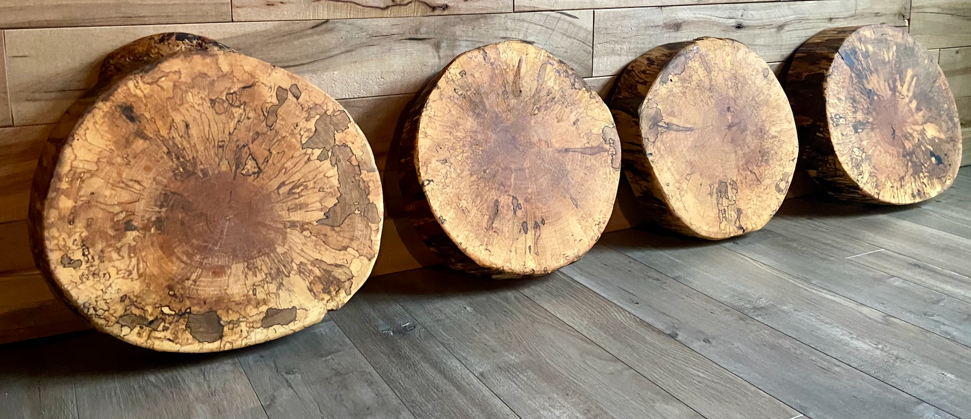 Four wooden stools with a natural finish on a wooden floor.