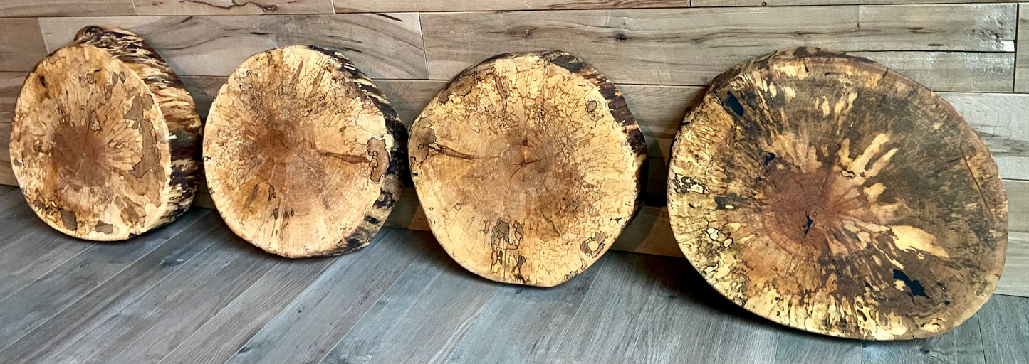 Four wooden table tops of different sizes arranged in a row on a wooden floor.