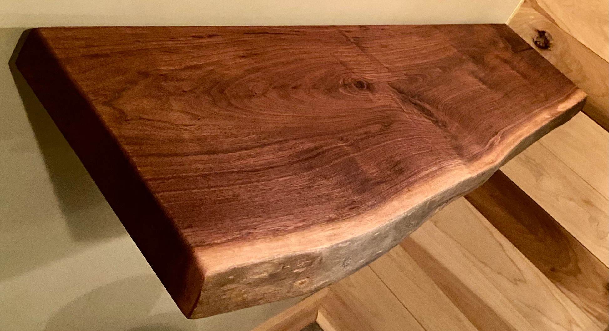 Live edge walnut floating shelf mounted on a light-colored wall, showcasing natural grain, dark tones, and organic edge detail. 