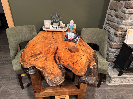 Wooden dining table with natural finish in a room with stone wall and gray chairs.