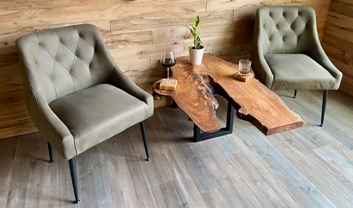 Two upholstered chairs around a rustic live edge english chestnut wooden table in a room with wooden walls and floor.