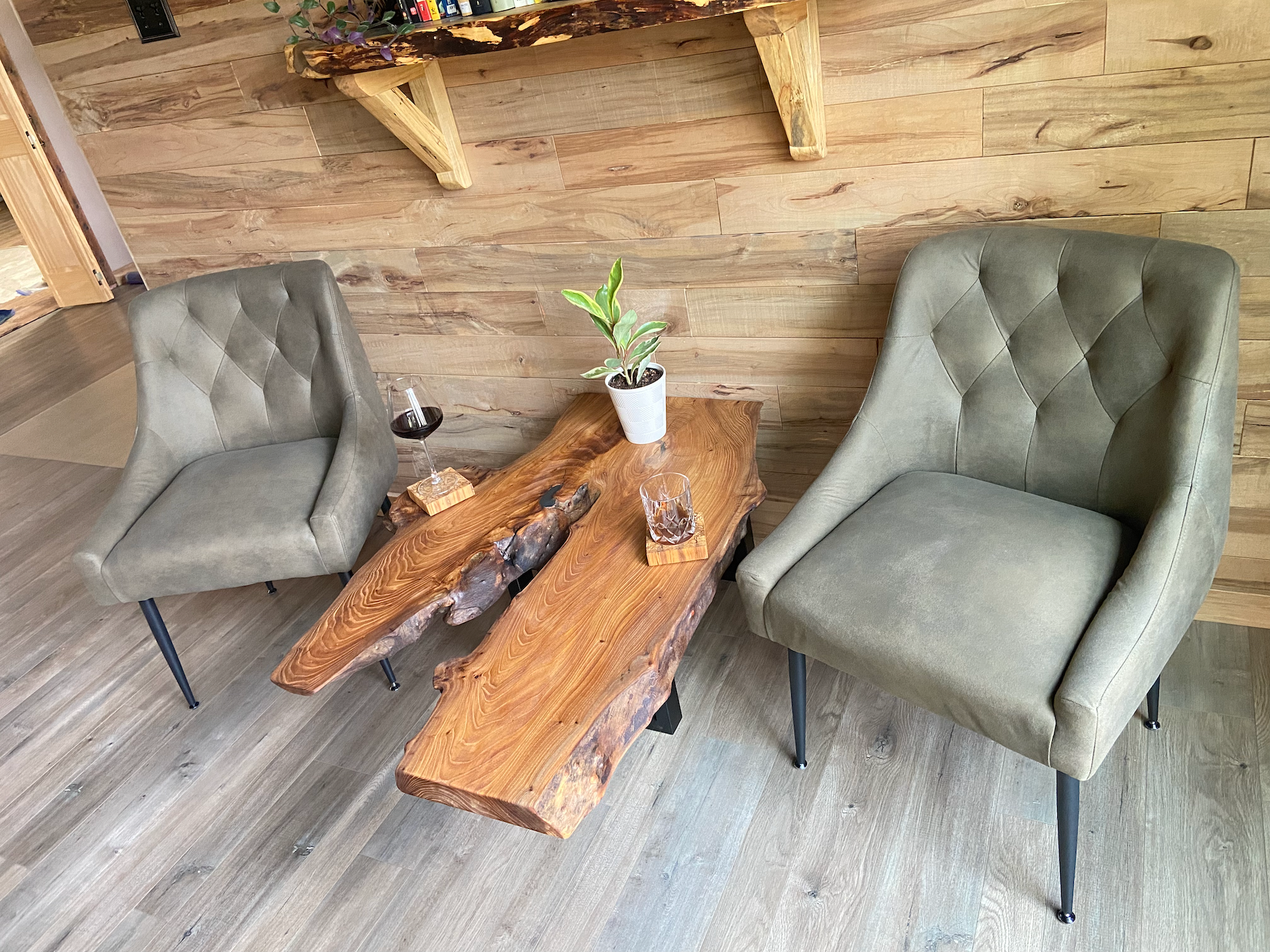 Two gray upholstered chairs with a wooden burl chestnut coffee table in a room with wooden walls and floor.