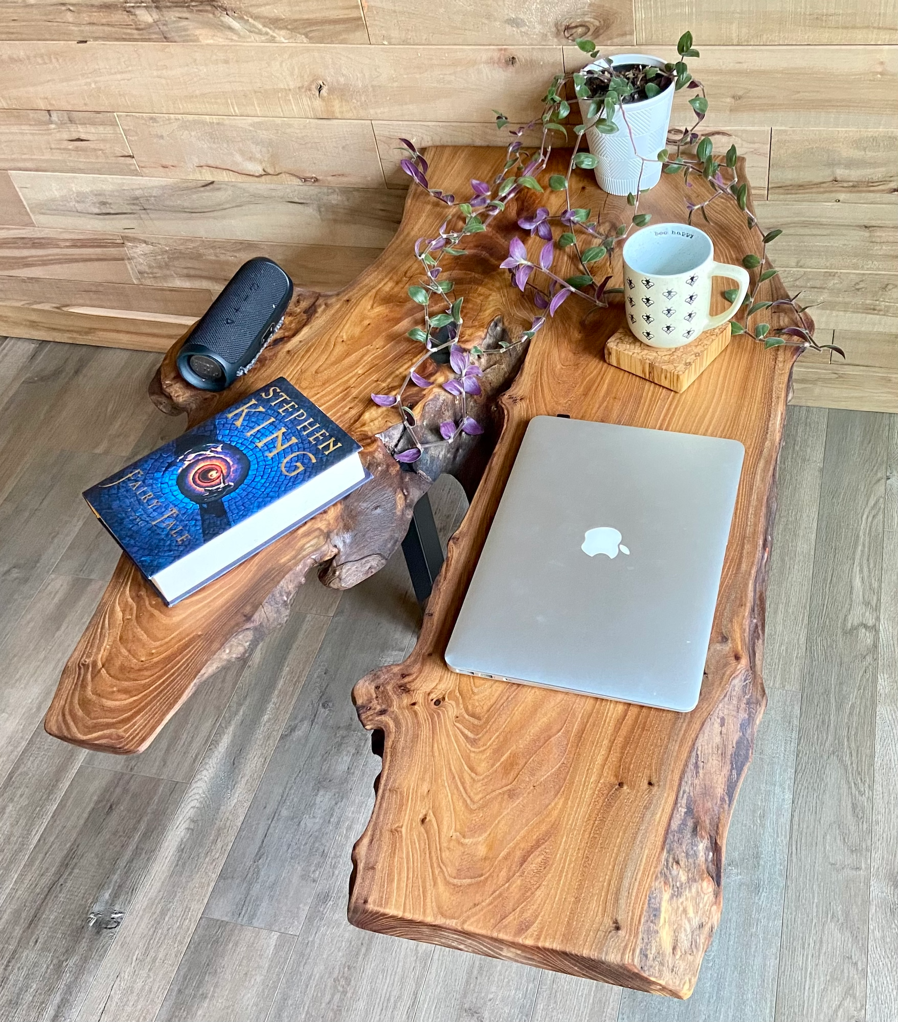 Wooden live edge chestnut coffee table with a laptop, book, and decorative items on a modern floor.