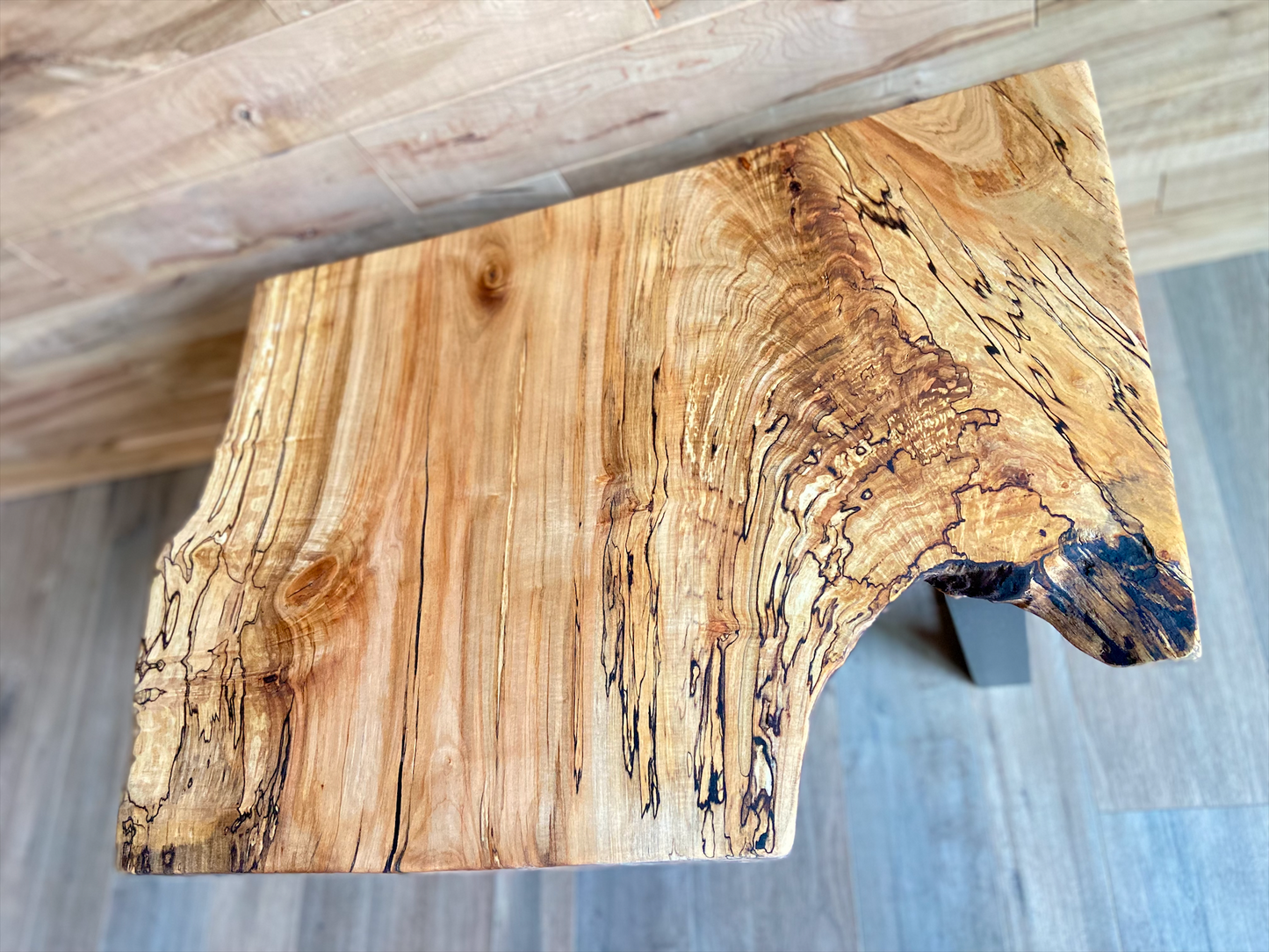 Wooden live edge maple end table with a natural grain pattern on a wooden floor.