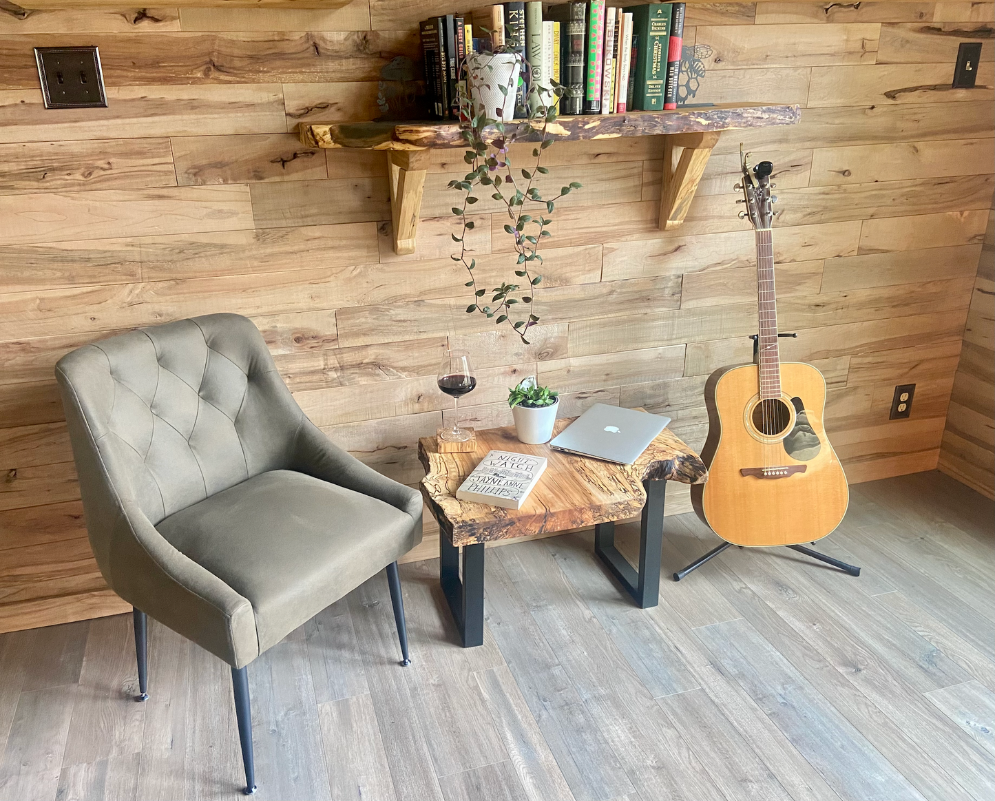 Cozy room with wooden wall, chair, live edge coffee table, guitar, and books on a live edge wooden shelf.