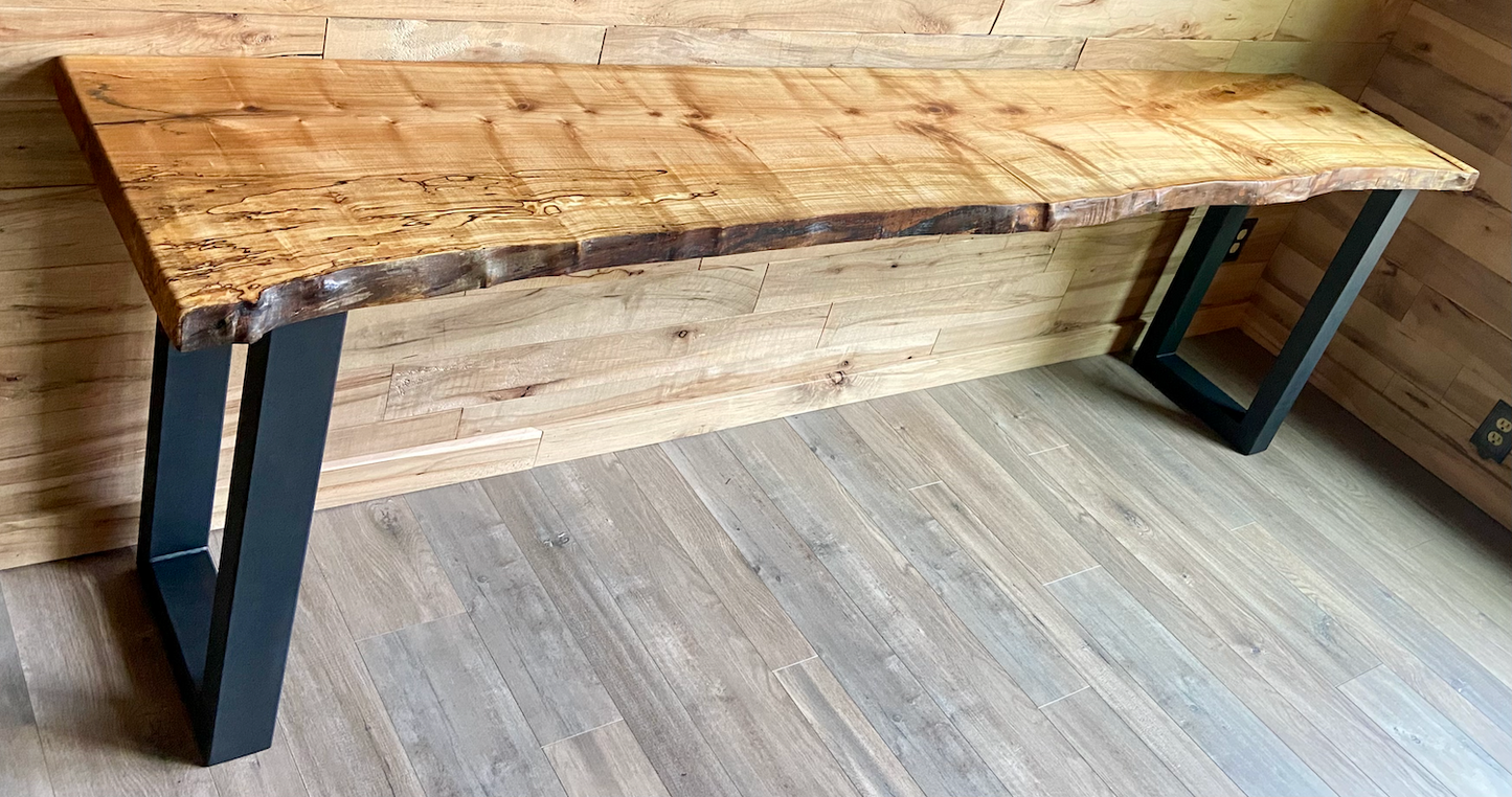 Wooden live edge maple sofa table with black metal legs in a room with wooden walls and floor.
