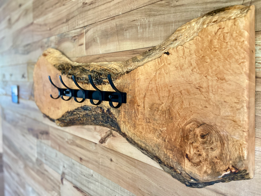 Live edge maple coat rack mounted on a wood-paneled wall, featuring 5 matte black metal hooks and natural wood grain patterns.