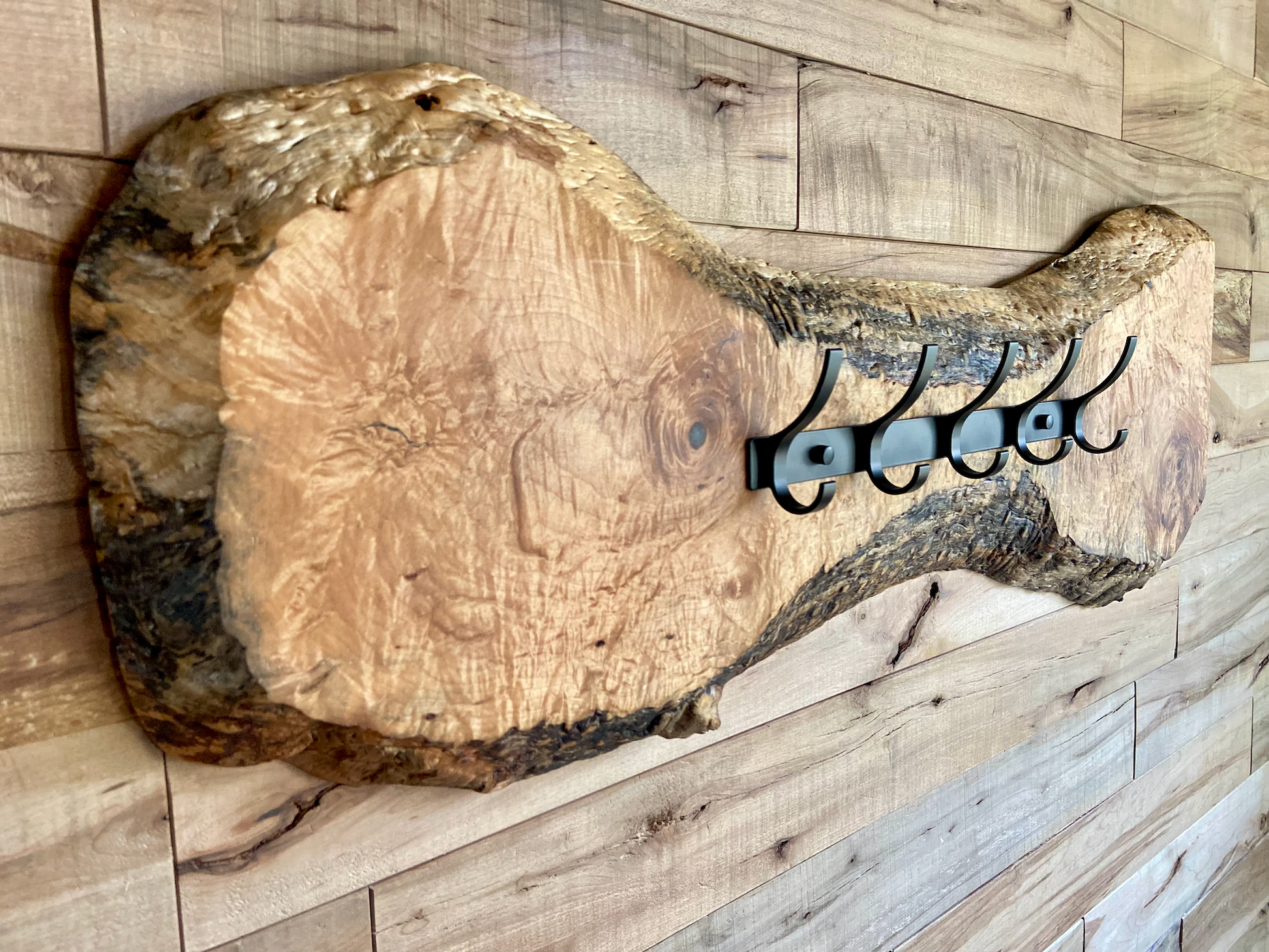 Live edge maple coat rack mounted on a wood-paneled wall, featuring 5 matte black metal hooks and natural wood grain patterns.