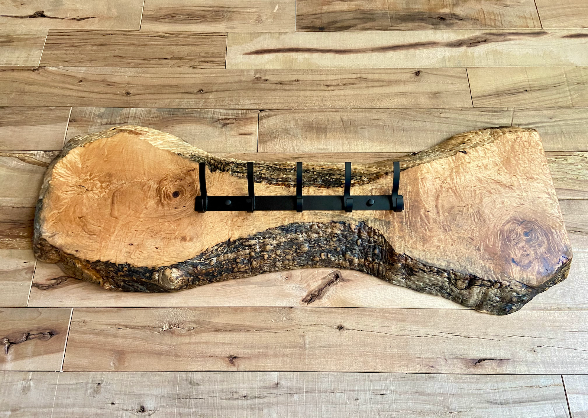 Live edge maple coat rack mounted on a wood-paneled wall, featuring 5 matte black metal hooks and natural wood grain patterns.