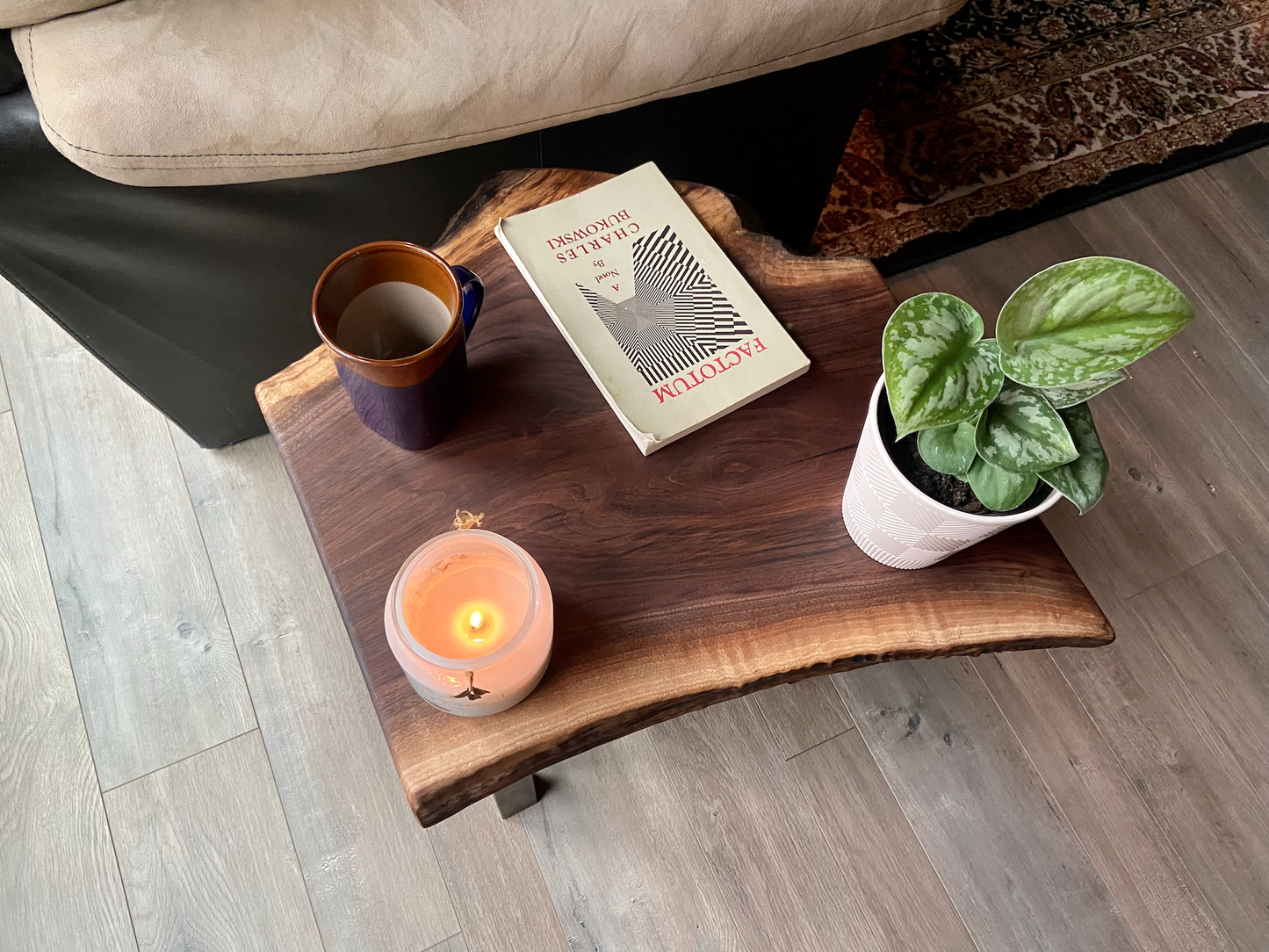 Top-down view of a live edge walnut side table with rich natural grain and smooth finish, set against a couch. Live edge walnut side table styled with everyday items, showing rustic charm and organic wood edge.