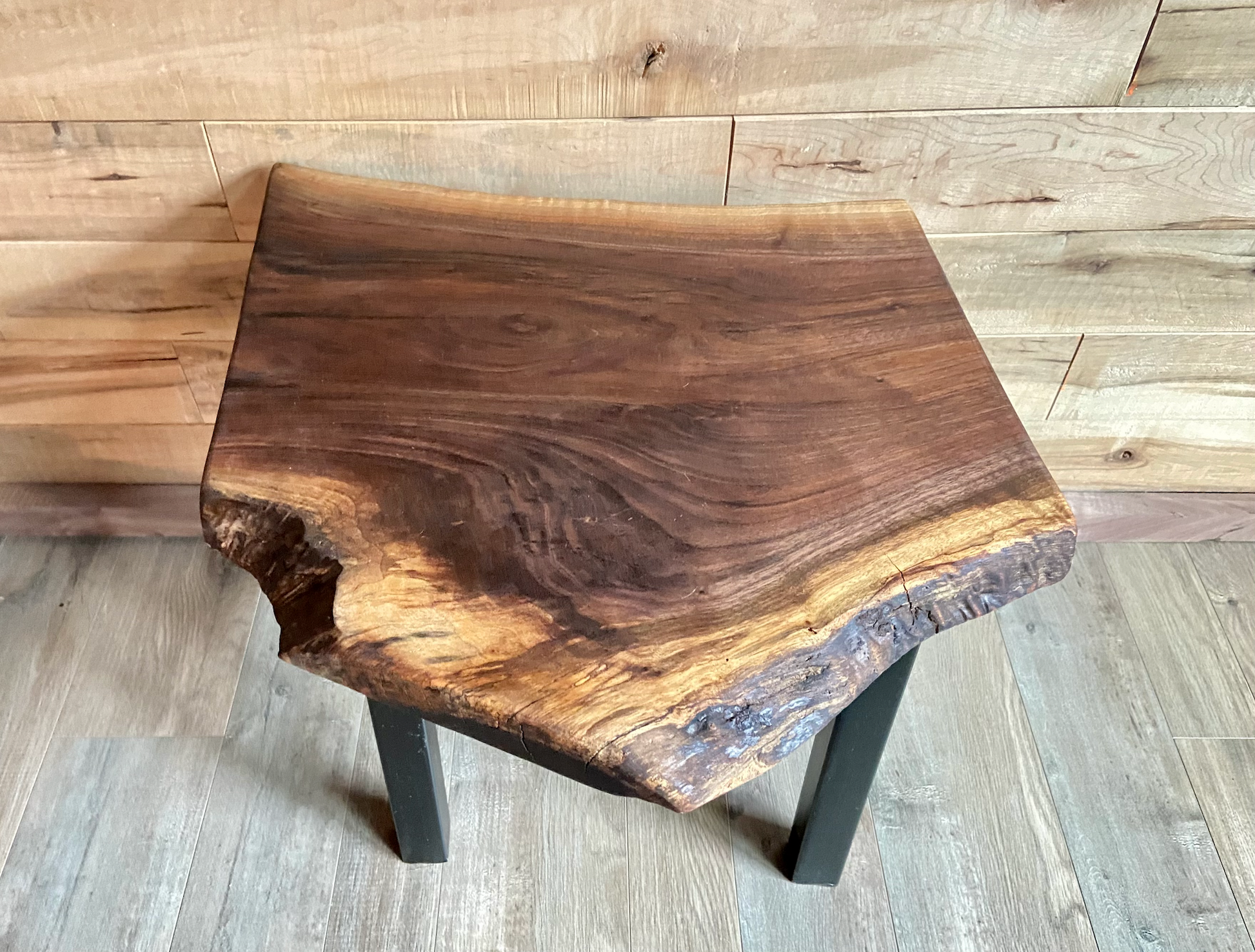 Top-down view of a live edge walnut side table with rich natural grain and smooth finish, set against a maple wall. Live edge walnut side table showing rustic charm and organic wood edge.