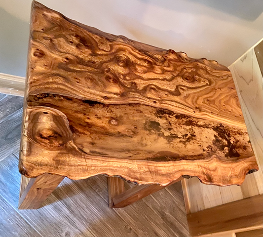 Wooden live edge chestnut coffee table with a natural, wavy grain pattern on a wooden floor.