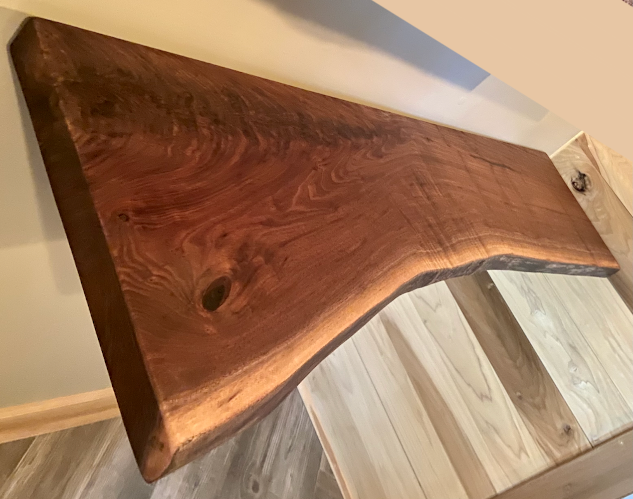 Live edge walnut floating shelf mounted on a light-colored wall, showcasing natural grain, dark tones, and organic edge detail