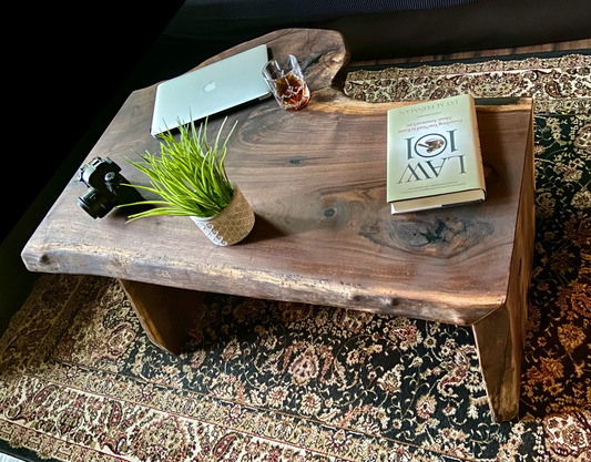 Top-down view of live edge black walnut waterfall wood coffee table with household items, highlighting natural wood grain, and live edge details. Handcrafted live edge walnut coffee table styled in a modern living room with a cozy, rustic aesthetic. Detailed view of walnut wood grain, showing natural color variations, and organic patterns. Live edge waterfall coffee table made from black walnut, featuring unique grain patterns and a smooth, polished surface. Rustic and modern design.