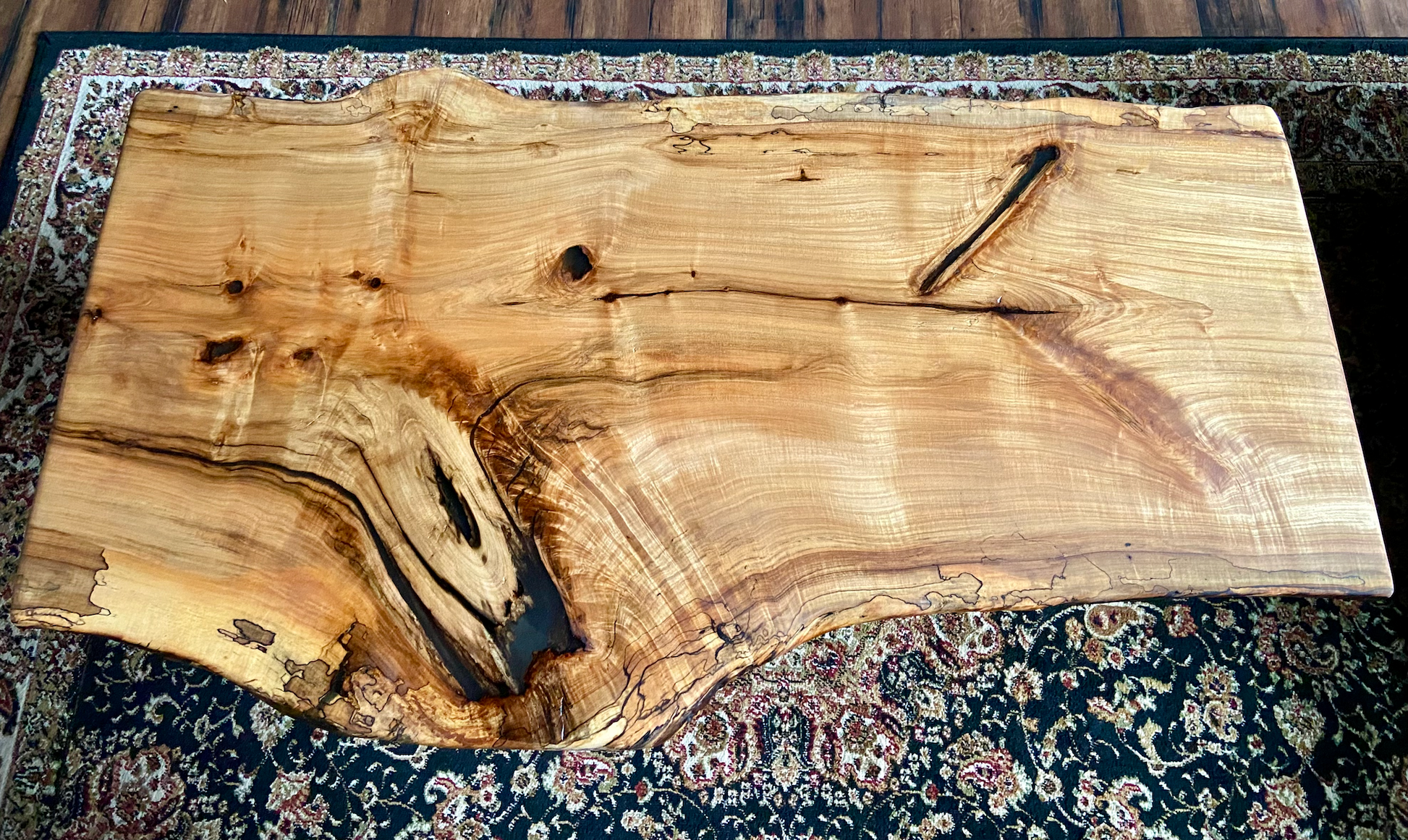 Wavy live edge spalted ambrosia maple wood slab coffee table with a natural grain pattern on a patterned rug.