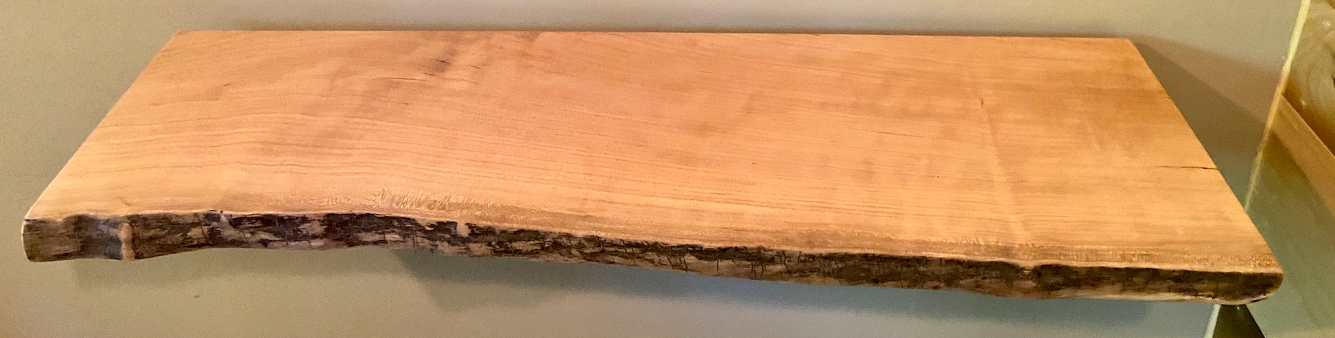 Live edge sycamore wood floating shelf mounted on a wall, showcasing natural grain and rustic edge detail.