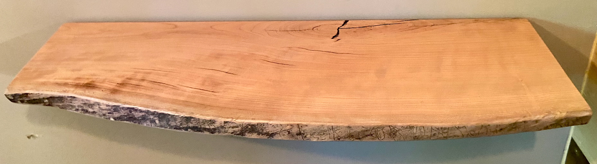 Live edge sycamore wood floating shelf mounted on a wall, showcasing natural grain and rustic edge detail.