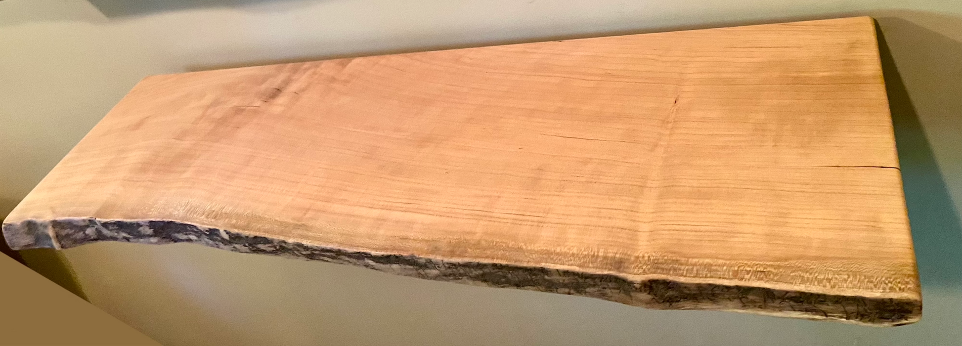 Live edge sycamore wood floating shelf mounted on a wall, showcasing natural grain and rustic edge detail.