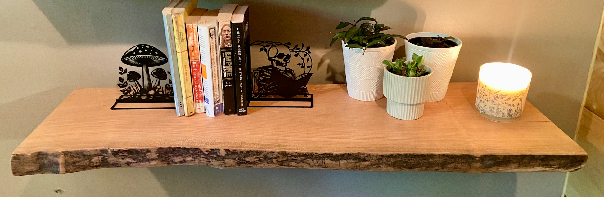 Rustic live edge sycamore shelf styled with books, metal bookends, potted plants, and a candle — ideal for modern farmhouse or nature-inspired interiors.