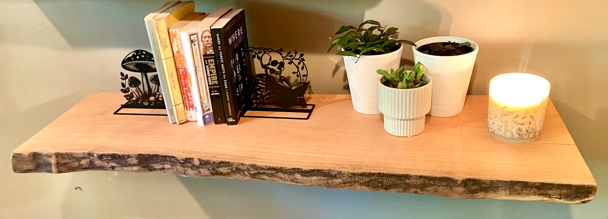 Rustic live edge sycamore shelf styled with books, metal bookends, potted plants, and a candle — ideal for modern farmhouse or nature-inspired interiors.