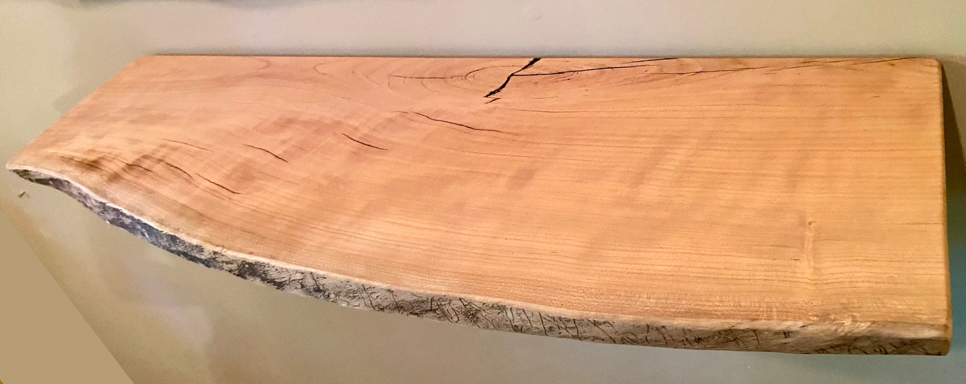 Live edge sycamore wood floating shelf mounted on a wall, showcasing natural grain and rustic edge detail.