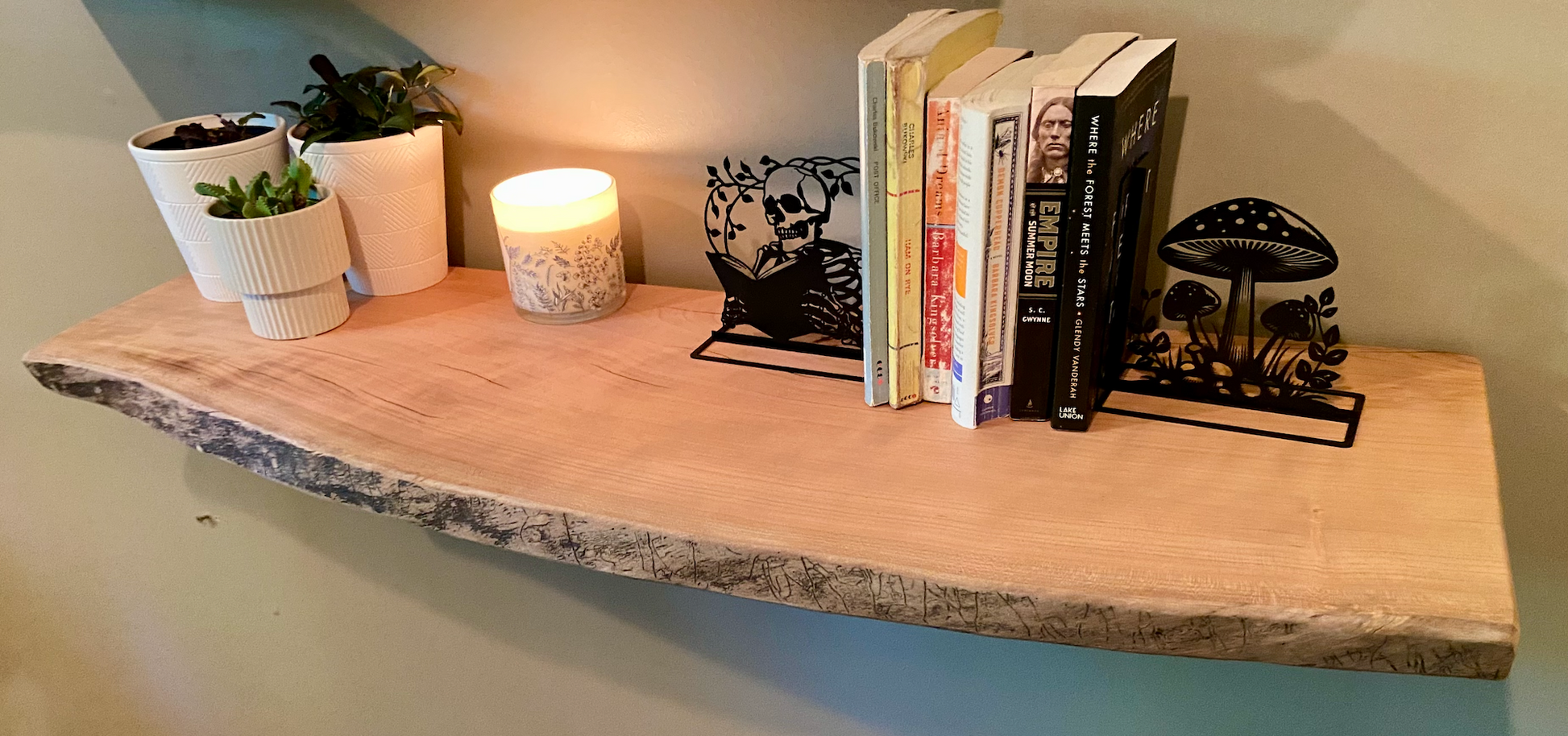 Rustic live edge sycamore shelf styled with books, metal bookends, potted plants, and a candle — ideal for modern farmhouse or nature-inspired interiors.