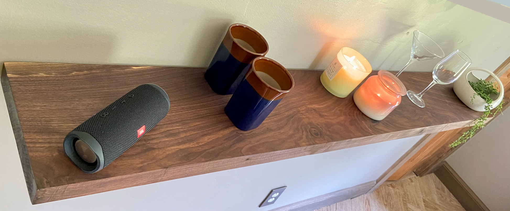 Front view of a handcrafted straight edge black walnut floating shelf mounted on a wall, displaying decorative items. Close-up of the solid black walnut wood grain, highlighting the shelf’s smooth finish. Side angle showcasing the shelf’s thickness and sturdy wall brackets.