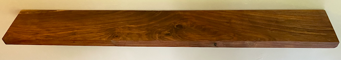 Front view of a handcrafted straight edge black walnut floating shelf mounted on a wall, displaying decorative items. Close-up of the solid black walnut wood grain, highlighting the shelf’s smooth finish. Side angle showcasing the shelf’s thickness and sturdy wall brackets.