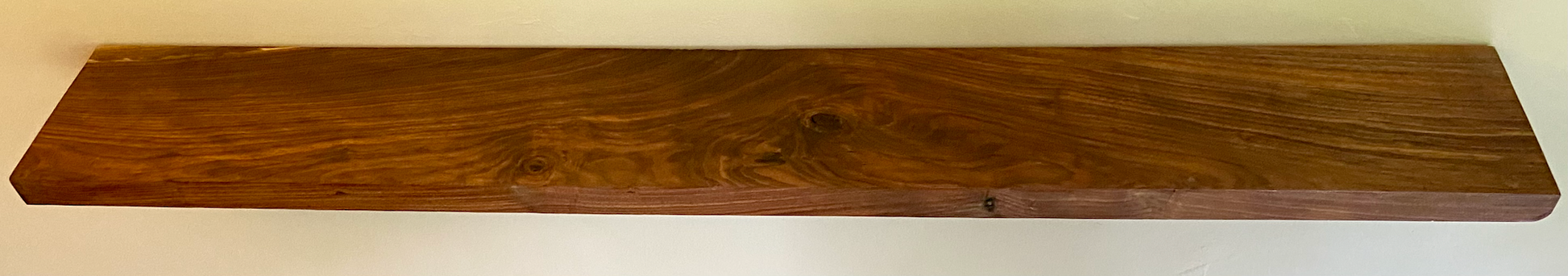 Front view of a handcrafted straight edge black walnut floating shelf mounted on a wall, displaying decorative items. Close-up of the solid black walnut wood grain, highlighting the shelf’s smooth finish. Side angle showcasing the shelf’s thickness and sturdy wall brackets.