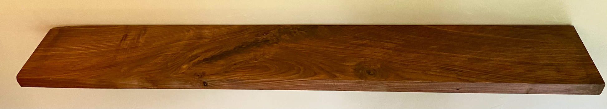 Front view of a handcrafted straight edge black walnut floating shelf mounted on a wall, displaying decorative items. Close-up of the solid black walnut wood grain, highlighting the shelf’s smooth finish. Side angle showcasing the shelf’s thickness and sturdy wall brackets.